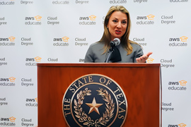 Secretary Hughs standing behind a podium. The Texas state seal is displayed on the podium. 