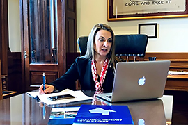 Secretary Hughs sitting at desk viewing a laptop screen.