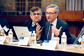 man is sitting at a table addressing the room. 