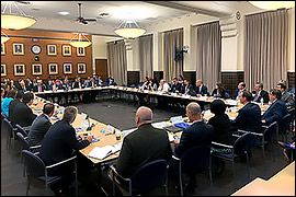 The BTAC members are all seated in a square formation in a large room facing each other.