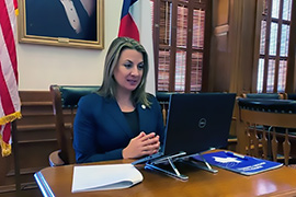 Secretary Hughs sitting at a desk in front of a computer.